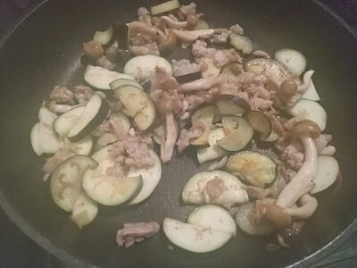 フライパンに豚こま肉を焼きなすとしめじも焼く写真