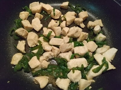 鶏肉をフライパンで炒めピーマンも入れて調味料で味付けする写真